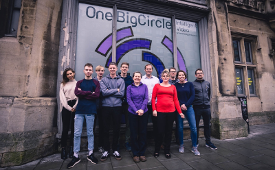 Team of 11 people standing outside one big circle building